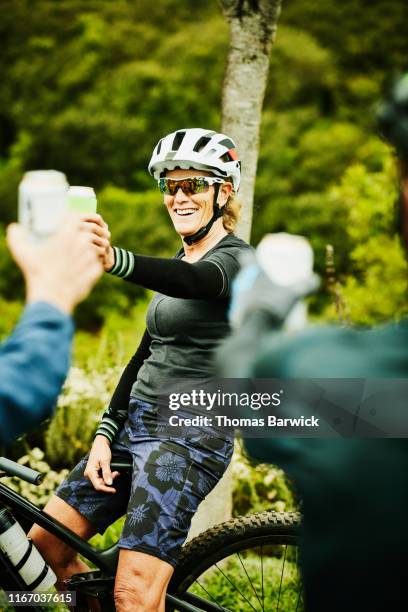 smiling mature woman toasting beers with friends after mountain bike ride - beer helmet stock pictures, royalty-free photos & images