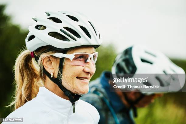 portrait of smiling mature woman resting during mountain bike ride with friends - vitaliteit fiets stockfoto's en -beelden