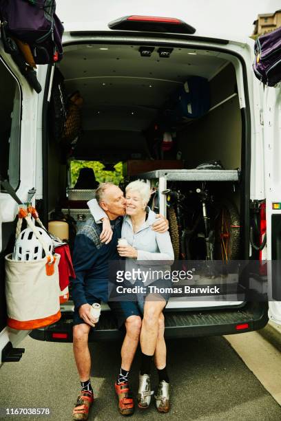 Senior man kissing wife at back of camper van after mountain bike ride