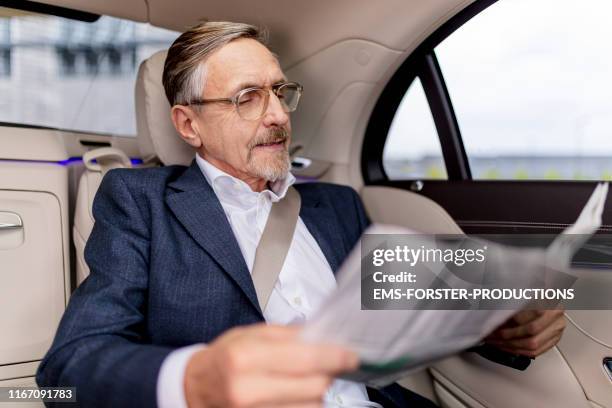 active senior sitting on back seat in car and reading newspaper - newspaper luxury bildbanksfoton och bilder