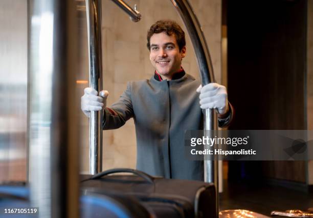 junger glockenjunge in einem hotel bewegt gepäckwagen in ein gästezimmer sehr fröhlich - concierge hotel stock-fotos und bilder