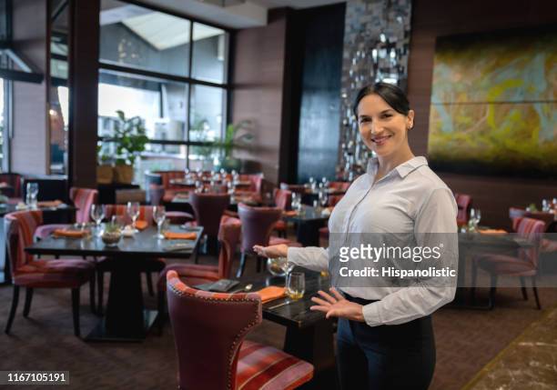 beautiful female hostess at a luxury hotel welcoming to restaurant while facing camera smiling - hostess stock pictures, royalty-free photos & images