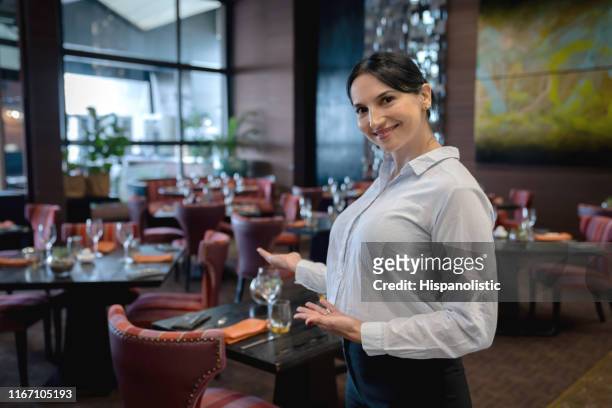 portret van vriendelijke gastvrouw in een hotel restaurant gastvrij met een hand gebaar en glimlachend op de camera - hostesses stockfoto's en -beelden