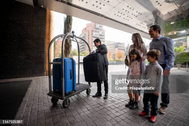 familia con dos niños llegando a un hotel de lujo y bellhop llevando maletas en el carro de equipaje - carrito-para-equipaje fotografías e imágenes de stock