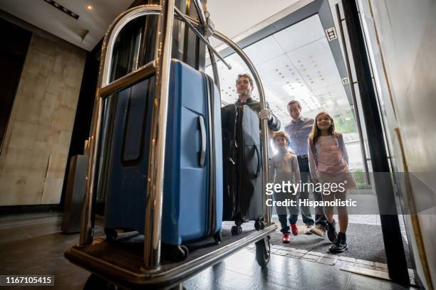 friendly bellhop pushing cart with guest family luggage on cart ready to check in into hotel - hotel stock pictures, royalty-free photos & images