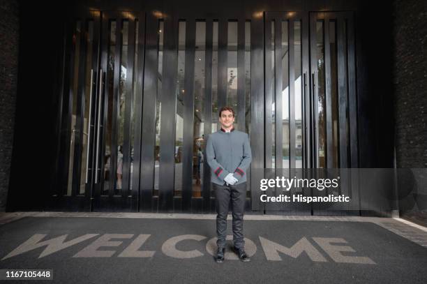friendly concierge standing at the entrance of a luxury hotel smiling at camera standing on a welcome mat - uniform imagens e fotografias de stock