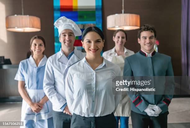 porträt von fröhlichen luxushotelmitarbeitern, die vor der kamera lächeln, und weiblicher betreuer, der im vordergrund steht - hotel uniform stock-fotos und bilder