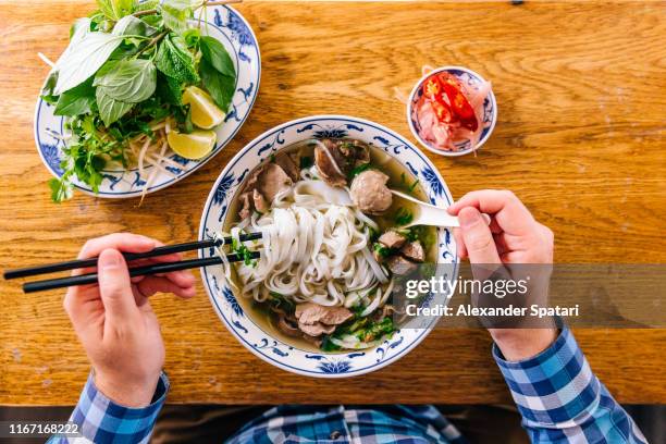 man eating vietnamese pho soup with noodles and beef, personal perspective view - pho suppe stock-fotos und bilder