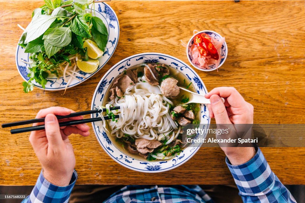 Man eating Vietnamese Pho soup with noodles and beef, personal perspective view