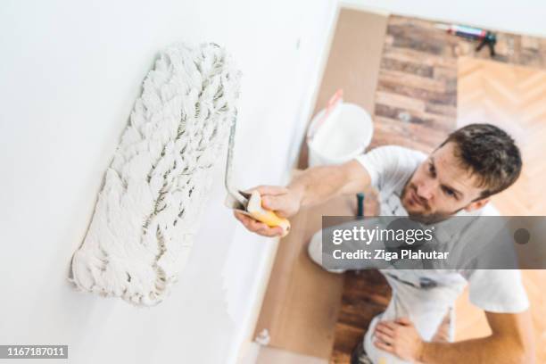 pittore professionista che tiene in mano un rullo di vernice immerso nella vernice bianca della parete - decorator foto e immagini stock