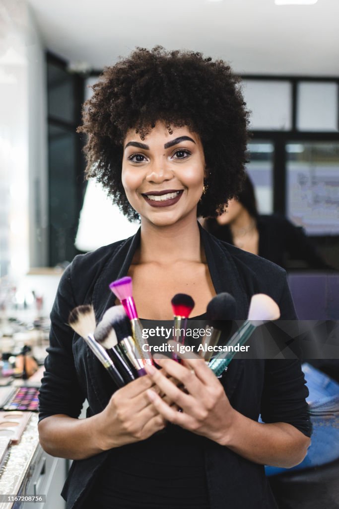 Portret van een lachende make-up artiest houden borstels