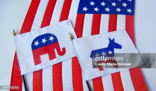 republican elephant and democratic donkey political party symbols on two small flags laying on the american flag. - partido-republicano-norteamericano fotografías e imágenes de stock