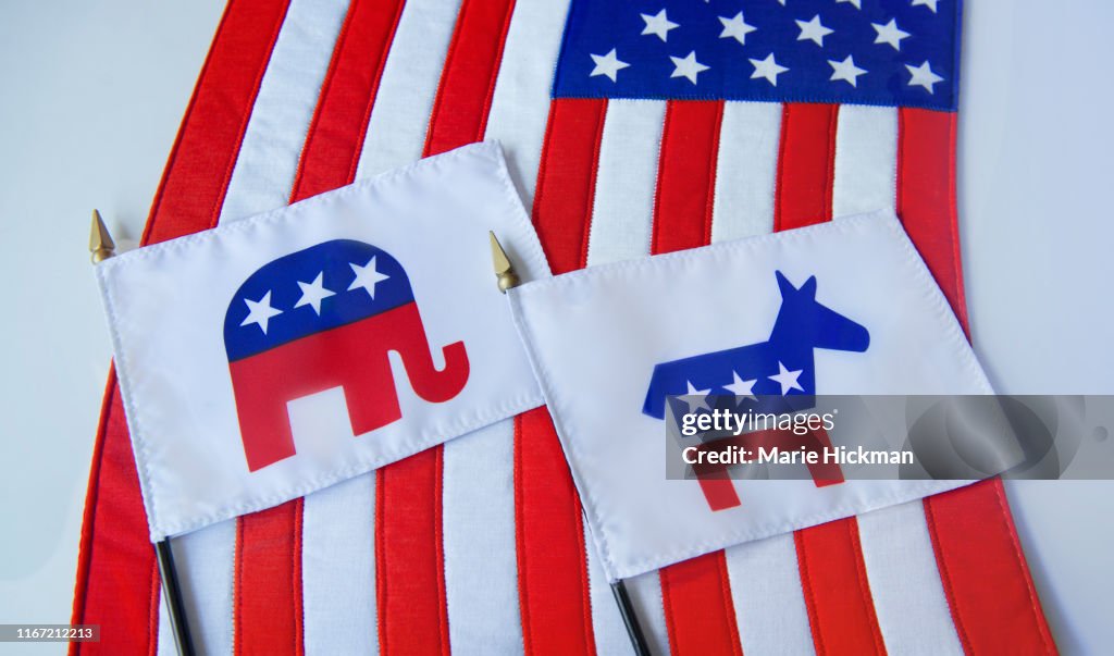 Republican Elephant and Democratic Donkey political party symbols on two small flags laying on the American Flag.