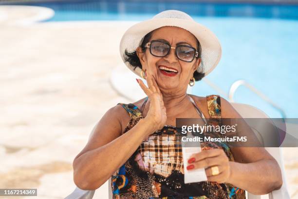 rijpe vrouw die zonneproducten lotion toepast - zonnehoed stockfoto's en -beelden