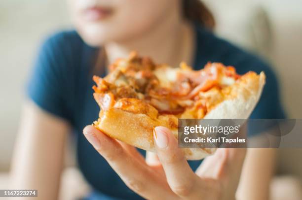 a young woman is spending her time eating a slice of pizza white sitting on a couch - salami stock pictures, royalty-free photos & images