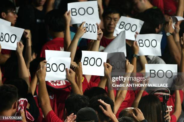 People turn their back and boo while holding up placards during the Chinese anthem at the start of the Qatar 2022 World Cup qualifying football match...