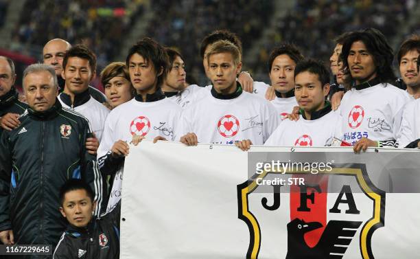 Japanese national team members and head coach Alberto Zaccheroni of Italy hold a banner before starting a charity match to raise money for victims of...