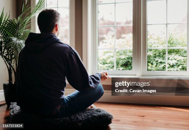 man sitting on the floor indoors meditating in front of windows. - zen man stock pictures, royalty-free photos & images