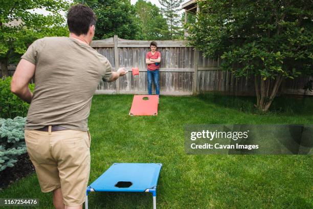 father and son playing corn hole game in the backyard together. - corn hole stock pictures, royalty-free photos & images