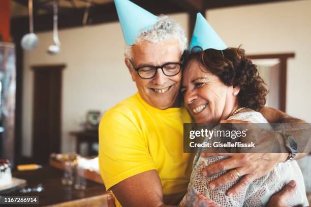 senior couple preparing a birthday party and embracing with love - senior birthday stock pictures, royalty-free photos & images