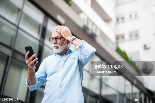 gefrustreerde senior man die slecht nieuws ziet op de telefoon. - frustration stockfoto's en -beelden