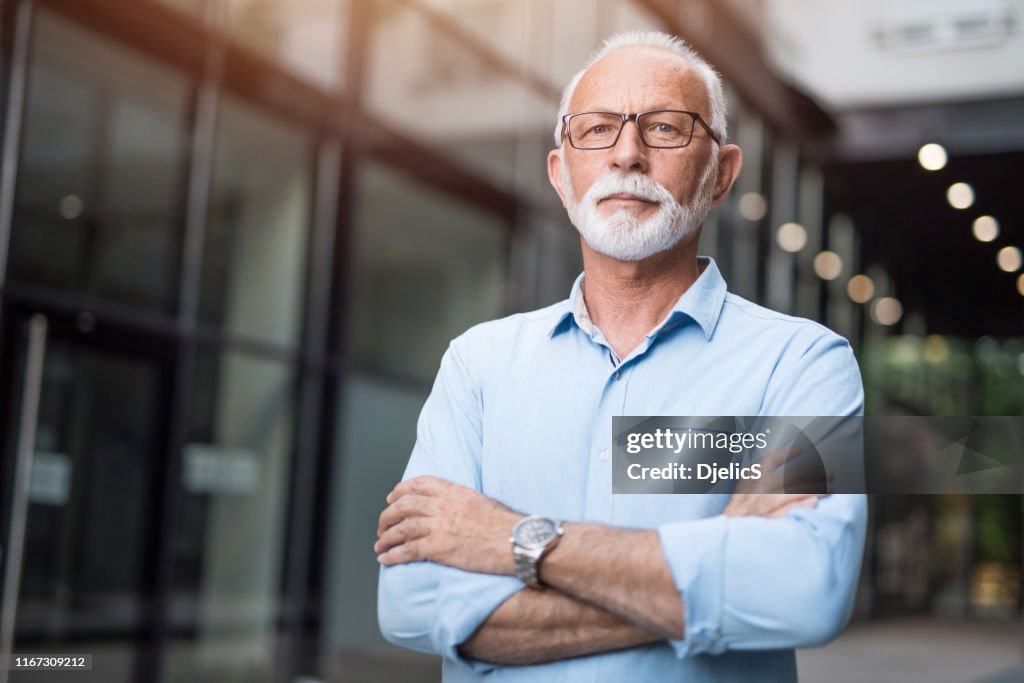 Senior businessman with arms crossed looking at camera.