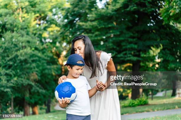mutter und sohn spielen fußball im öffentlichen park - gemeinsam gehen stock-fotos und bilder