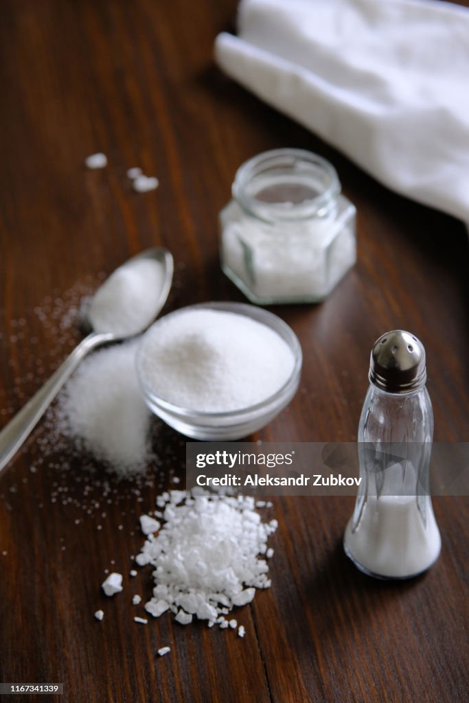 Natural, organic, sea, white salt in a spoon, in a Cup, in a salt shaker, poured on a wooden table. Next to the linen towel. The concept of cooking healthy food, cosmetology. Selective focus