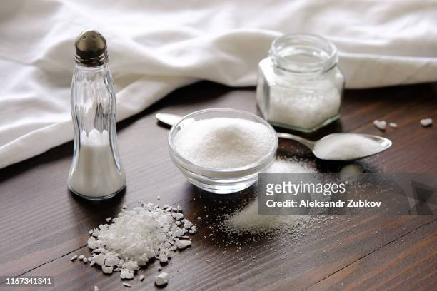 natural, organic, sea, white salt in a spoon, in a cup, in a salt shaker, poured on a wooden table. next to the linen towel. the concept of cooking healthy food, cosmetology. selective focus - zout smaakstof stockfoto's en -beelden