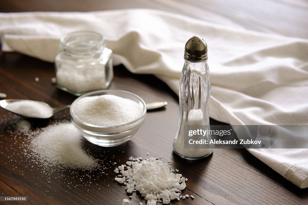 Natural, organic, sea, white salt in a spoon, in a Cup, in a salt shaker, poured on a wooden table. Next to the linen towel. The concept of cooking healthy food, cosmetology. Selective focus