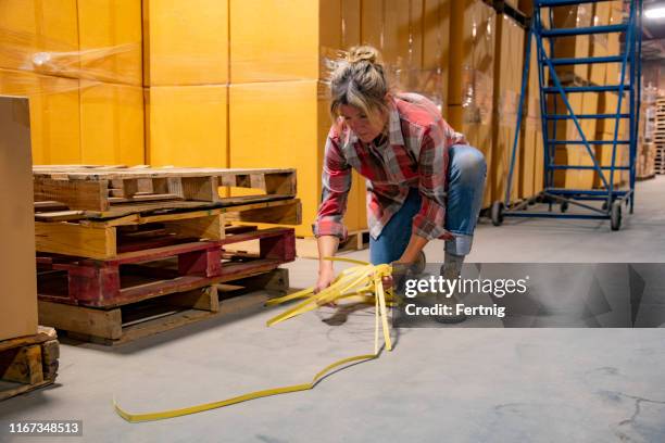 an industrial warehouse workplace safety topic.  a woman cleaning-up a trip hazard in a warehouse. - trip hazard stock pictures, royalty-free photos & images