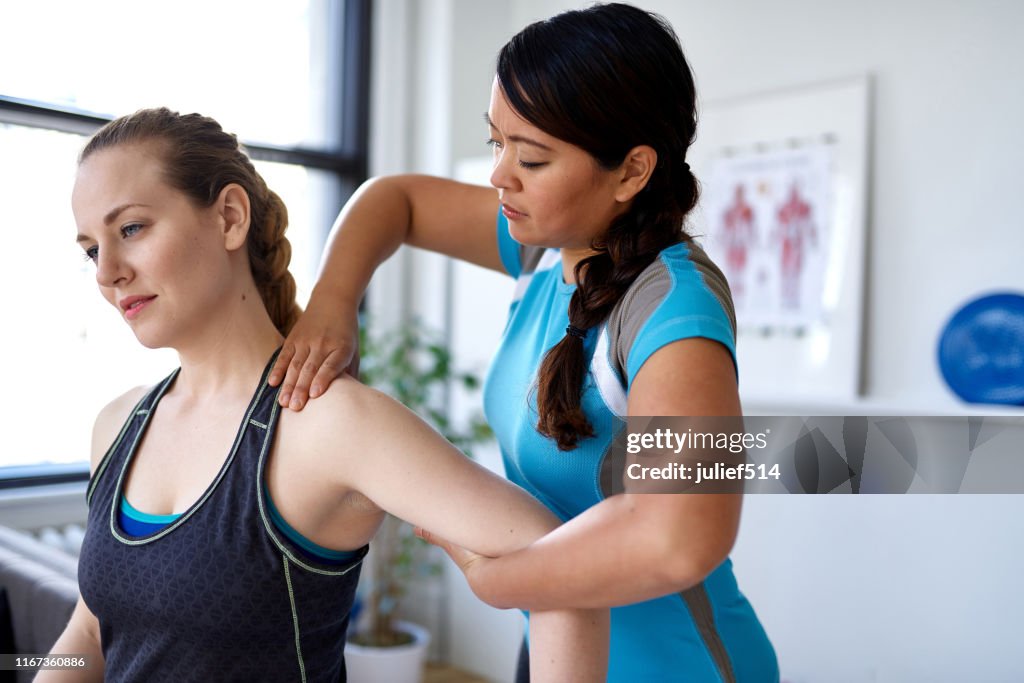 Chinese woman physiotherapy professional giving a treatment to an attractive blond client in a bright medical office