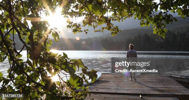 man walks onto dock over lake and watches sunrise over mountains and forest - distant forest stock pictures, royalty-free photos & images