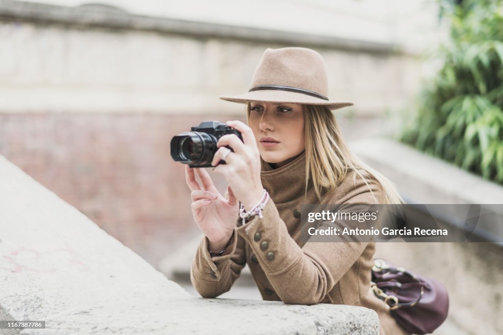 Woman well dressed taking pictures in street with hat and raincoat in park