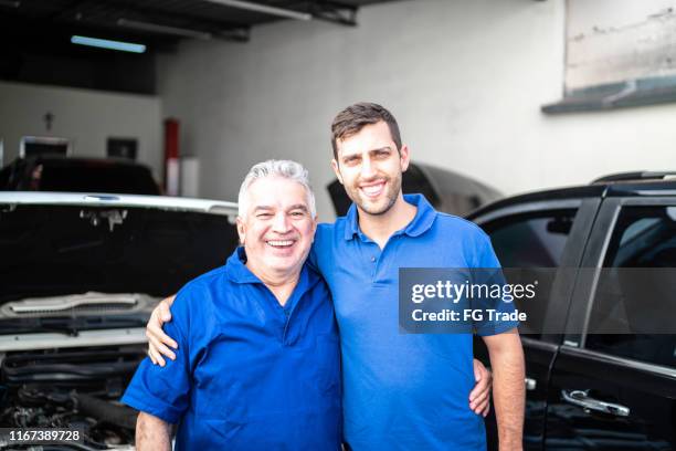 portrait of two mechanics standing in a repair shop (family business) - family business generations stock pictures, royalty-free photos & images