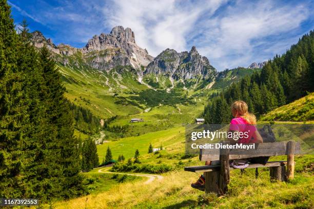 a mulher nova que senta-se no banco e aprecia a vista em bischofsmütze grande, montanhas de dachstein, alpes - salzkammergut - fotografias e filmes do acervo