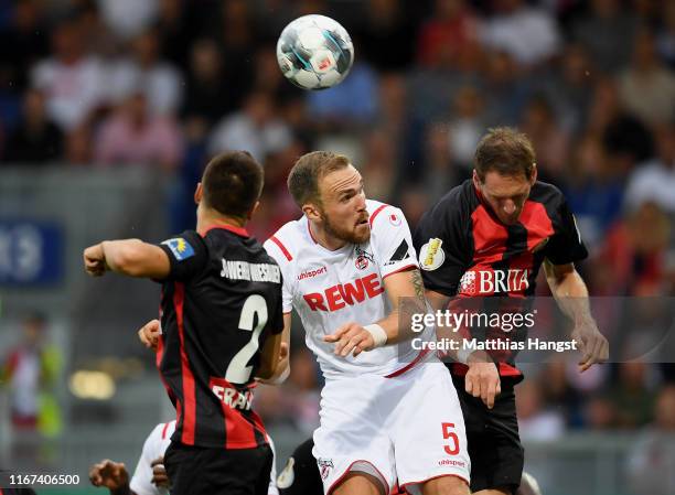 Rafael Czichos of 1. FC Koeln jumps for a header with Dominik Franke of SV Wehen Wiesbaden and Benedikt Roecker of SV Wehen Wiesbaden during the DFB...