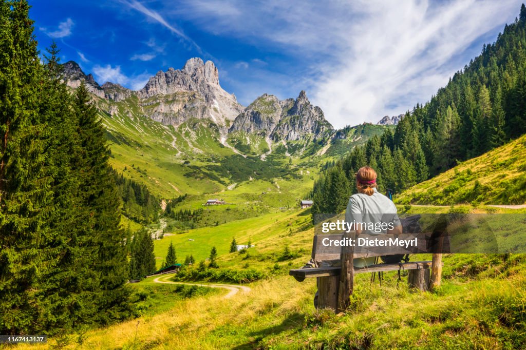Young man sitting on bench and enjoys view on big Bischofsmütze, Dachstein mountains, alps