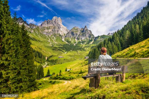 o homem novo que senta-se no banco e aprecia a vista em bischofsmütze grande, montanhas de dachstein, alpes - salzkammergut - fotografias e filmes do acervo