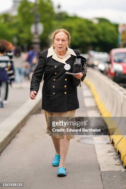 Guest wears earrings, a pearl necklace, a double-breasted black Chanel jacket with a cream-color collar, a white camellia brooch, a black quilted...