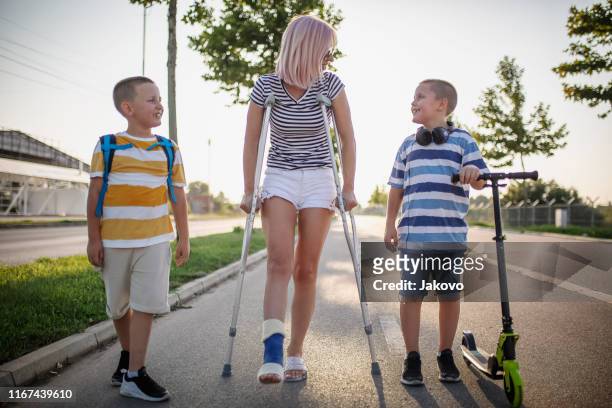 madre con sus hijos caminando usando muletas - pierna fracturada fotografías e imágenes de stock