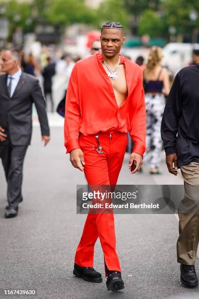Russell Westbrook wears necklaces, an orange shirt, red pants, black sneakers, LV keyholder, outside Vuitton, during Paris Fashion Week - Menswear...