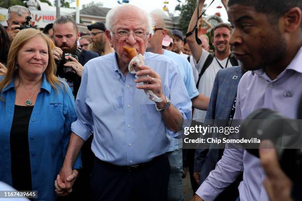 Democratic presidential candidate munches on a corn dog as he and his wife Jane O'Meara Sanders walk around the Iowa State Fair August 11, 2019 in...