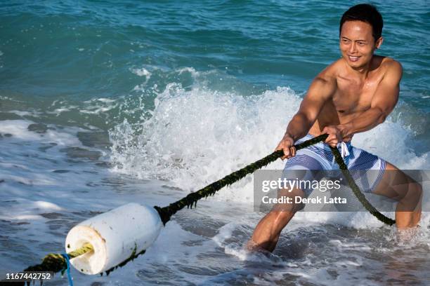 attractive confident asian man of filipino descent pulling on a rope in the ocean. - 綱引き ストックフォトと画像