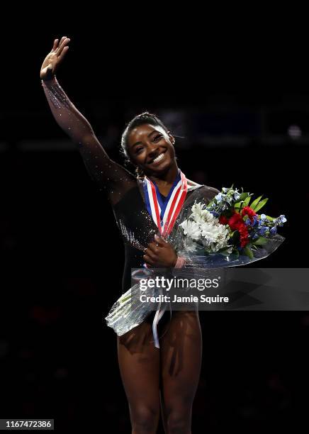 Simone Biles waves from the podium after winning the all-around gold medal during Women's Senior competition of the 2019 U.S. Gymnastics...