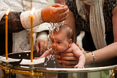 Newborn baby baptism in Holy water. baby holding mother's hands. Infant bathe in water. Baptism in the font
