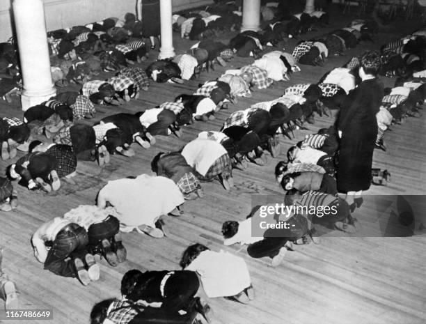 Teacher supervises schoolchildren kneeling, arms crossed and head on the floor during an anti-atomic exercise, on December 1952 in the United States.