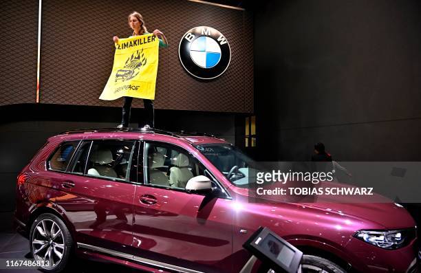 Greenpeace activist standing on a BMW car holds a poster reading "Climate Killers" as she demonstrates at the booth of German car maker BMW, where...