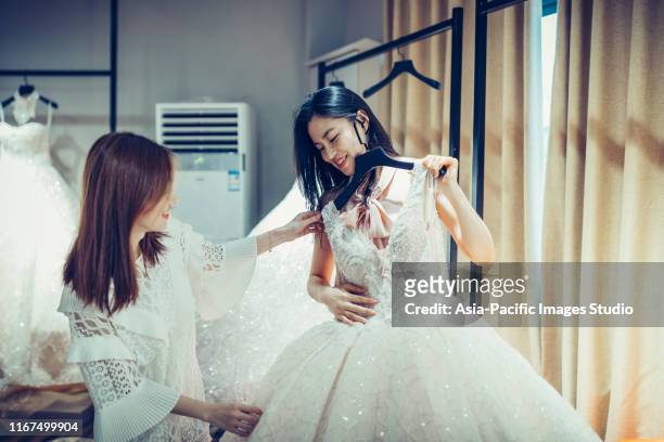 deux jeunes femmes asiatiques faisant des emplettes pour des robes de robe de mariage dans le magasin de bon marché de boutique, beaucoup de vêtements blancs accrochant sur la rangée de cintres de rack. - wedding dress photos et images de collection
