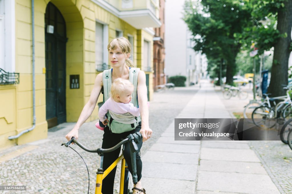 Young mother with baby in the carrier riding the bike through the city